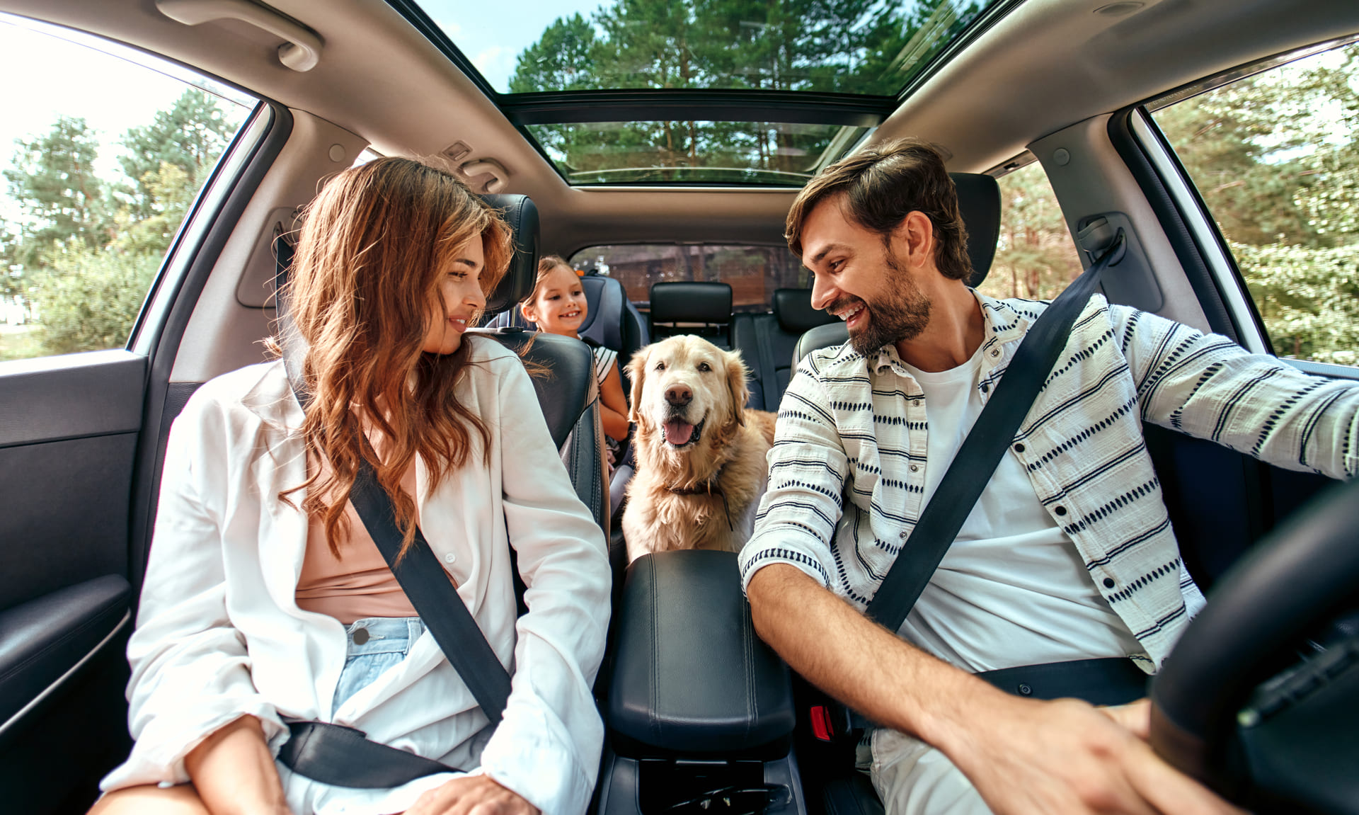Семья с ребенком и собакой едет в собственной машине. Они рады, что собрались все вместе
